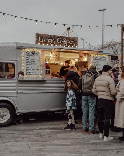 People gather at a cozy Christmas market in Zürich, enjoying crepes from a vintage food truck adorned with lights.