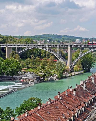 Panoramic view of the historic Kirchenfeld Bridge over the Aare River in Bern, surrounded by lush greenery and traditional rooftops.