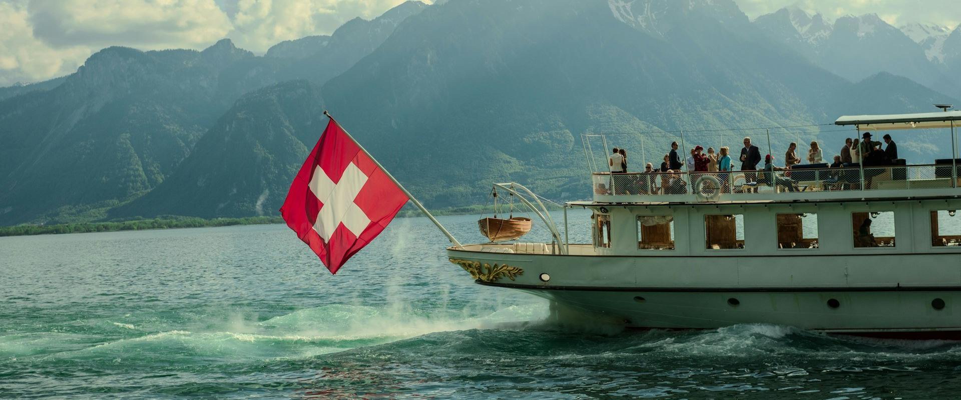 A swiss boat cruises on a lake near mountains.